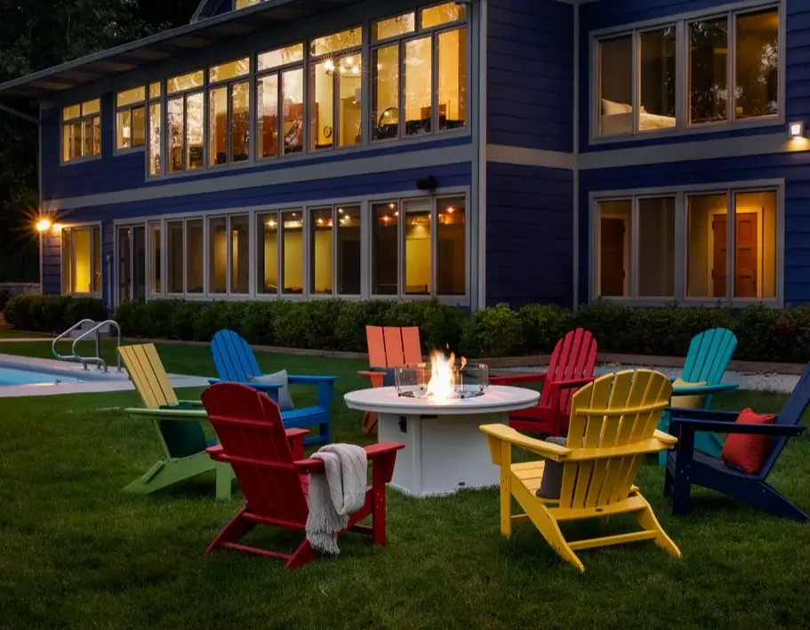 Colorful Adirondack chairs surrounding a fire pit beside a pool, creating a welcoming outdoor gathering space for guests.